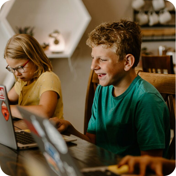Two children sitting at a table using laptops